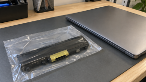 An intact laptop battery pack in an individual clear bag beside a closed laptop