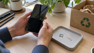 Hands holding a smartphone beside a SIM tray and eject tool on a desk