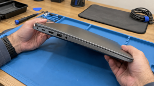 Hands examining a used business laptop on an electronics workbench
