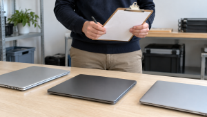 Hands holding a clipboard beside three closed laptops on an office table