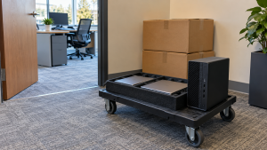 Laptops and a desktop computer on a cart near an office doorway and moving boxes